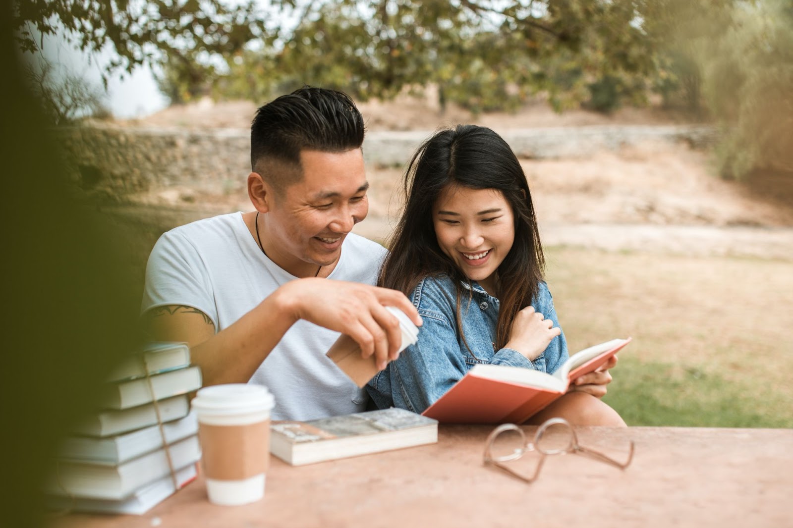 Asian couple sitting outside at a table reading a book together