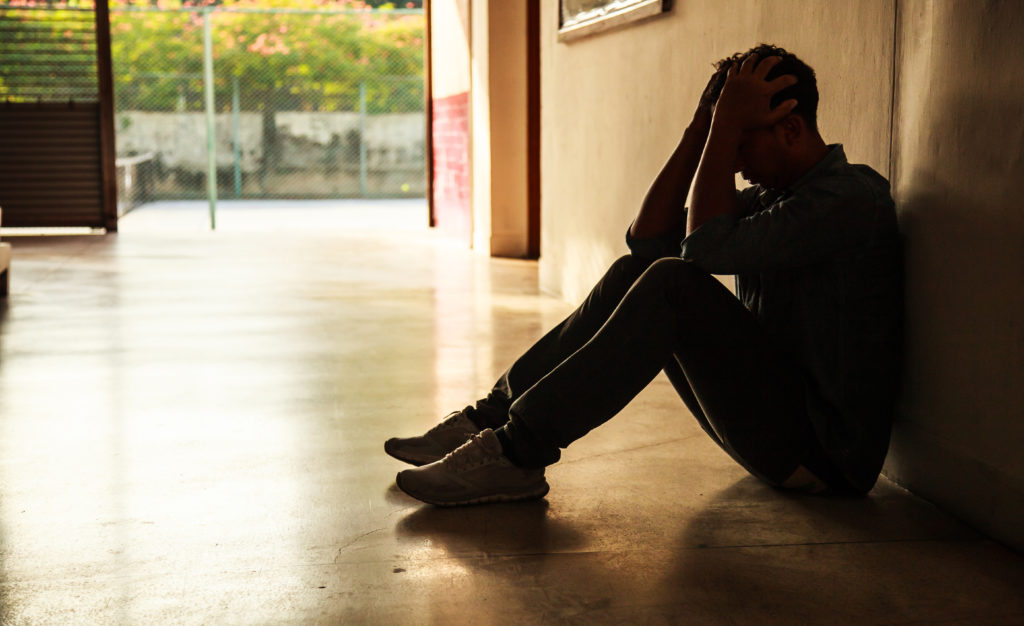 Emotional moment: man sitting holding head in hands, stressed sad young male having mental problems, feeling bad, depressed, disappointed, hopeless. Desperate man in the dark corner needing help.