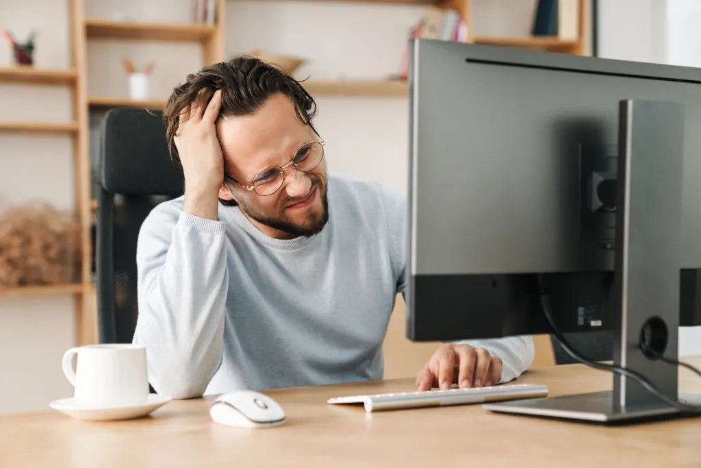 Image of unhappy bearded programmer man wearing eyeglasses working with computer in office