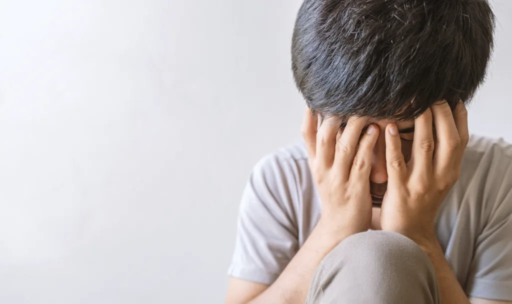 closeup man sitting alone felling sad worry regret or fear and hand off his face in the room. soft-focus and over light in the background