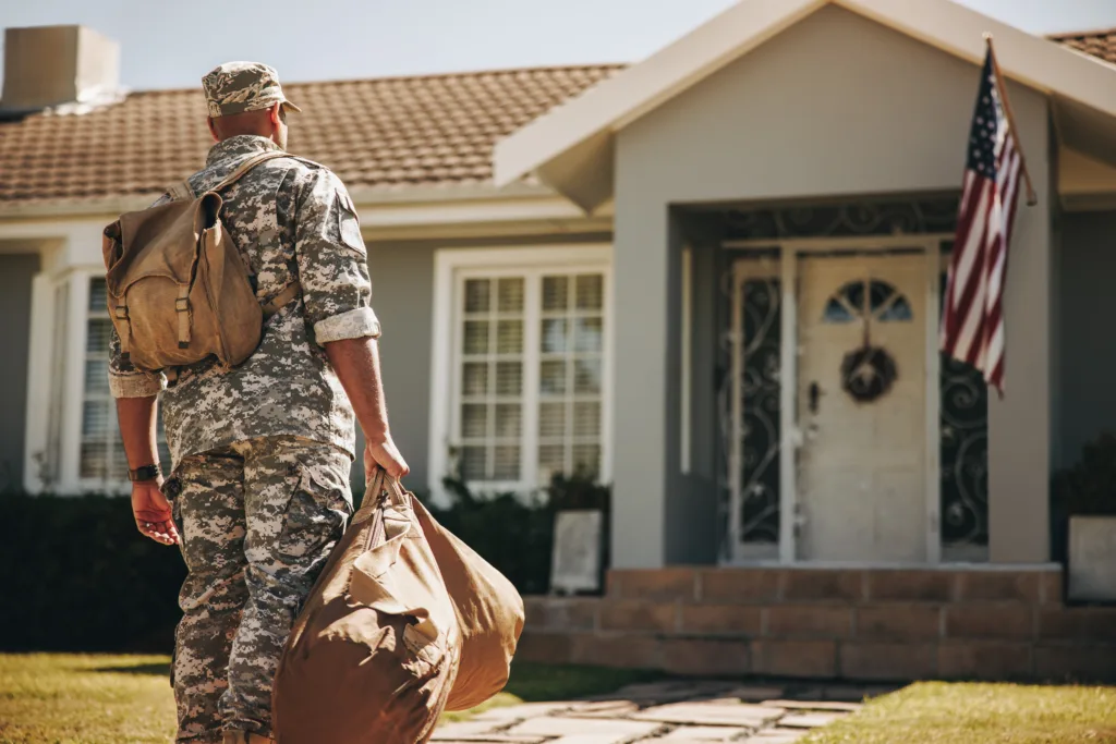 Back view of a courageous young soldier walking towards his house with his luggage. American serviceman coming back home after serving his country in the military.