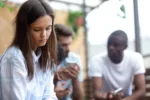 girl sitting outside with friends but looking down at her feet sad